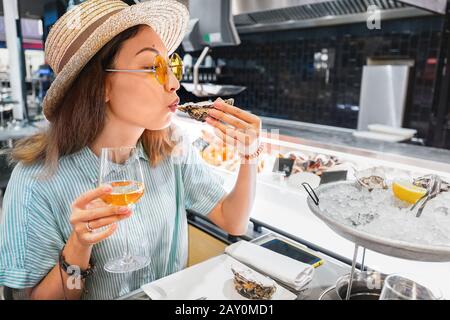 Asiatische Frau schmeckt frischen Rohauster und trinkt Wein im Fischrestaurant Stockfoto