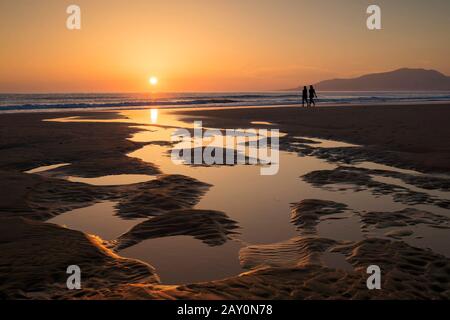 Silhouette zweier Frauen, die bei Sonnenuntergang am Strand spazieren, Tarifa, Cadiz, Andalusien, Spanien Stockfoto