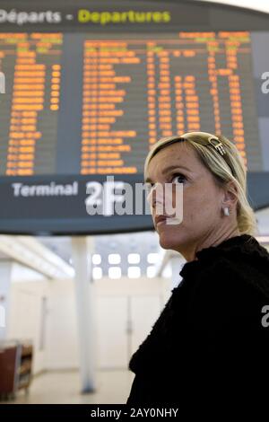 Eine Frau steht vor einem großen Brett mit Abfluginformationen in der Abflughalle von Terminal 2 und blickt über sie Stockfoto