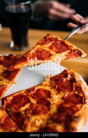 Menschliche Hand, die eine Scheibe Pfefferoni Pizza serviert Stockfoto