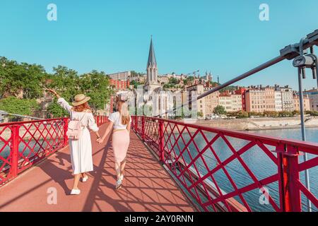 Zwei glückliche Mädchen-Freunde, die auf der Fußgängerbrücke Saint Georges spazieren gehen, während sie in der französischen Altstadt von Lyon unterwegs sind Stockfoto