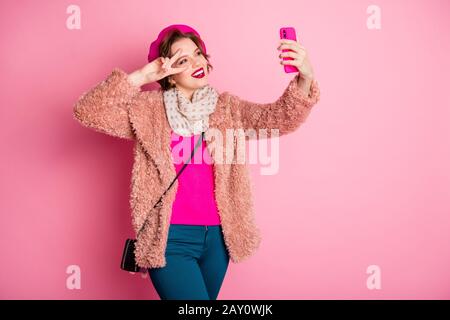 Foto der hübschen Reisenden Dame Telefon mit lustigen Selfies mit V-Zeichen in der Nähe Auge Flirty tragen Freizeit stylischer Fellmantel Schal Beret-Hose Stockfoto