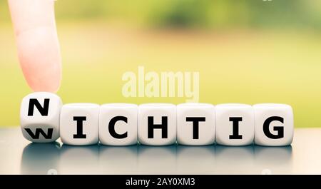Hand dreht Würfel und ändert das deutsche Wort "wichtig" ("wichtig") in "nichtig" ("unwichtig"). Stockfoto