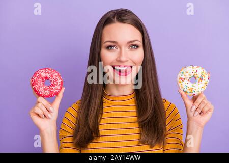 Nahporträt von ihr hübsches hübsches hübsches fröhliches fröhliches Mädchen, das zwei bunte Donuts in den Händen hält, die die Lippe isoliert lecken Stockfoto