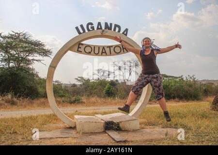 North South Boundary Mark - Äquator im Queen Elizabeth National Park in Uganda und ein fröhliches kaukasisches europäisches Touristenmädchen springen. Stockfoto