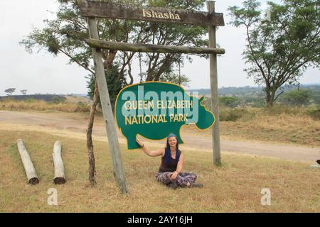 Junge Frau Touristin sitzt unter dem Zeichen des Queen Elizabeth National Park in Uganda. Stockfoto