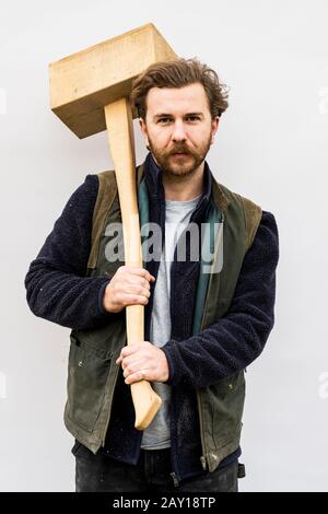 Porträt eines bärtigen Mannes, der Holzklotz vor weißem Hintergrund hält und die Kamera betrachtet. Stockfoto