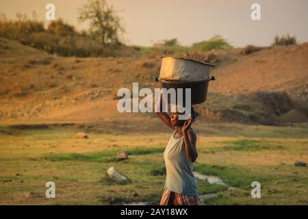 Kampala, Uganda - 17. Februar 2015: Afrikanische Dorffrau trägt bei Sonnenuntergang in der Savanne ein Wasserbecken auf dem Kopf. Stockfoto