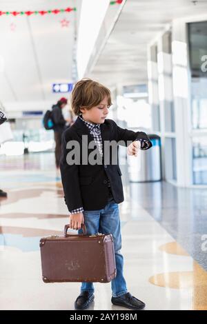 6 Jahre alter Junge, der seine Uhr am Flughafen betrachtet Stockfoto