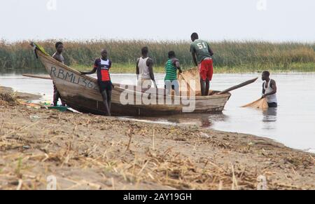 Fort Portal, Uganda - 17. Februar 2015: Eine Gruppe junger schwarzer afrikanischer Teenager aus einer armen Provinz schleppen ein Boot ans Ufer, um sich auf Fisch vorzubereiten Stockfoto