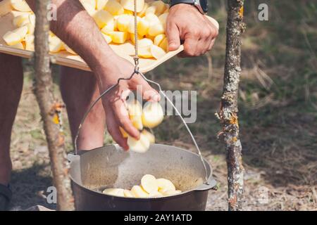 Männliche Hand fügt Kartoffel in einem Kessel hinzu. Zubereitung einer Suppe im offenen Feuer, Campingmahlzeit Stockfoto