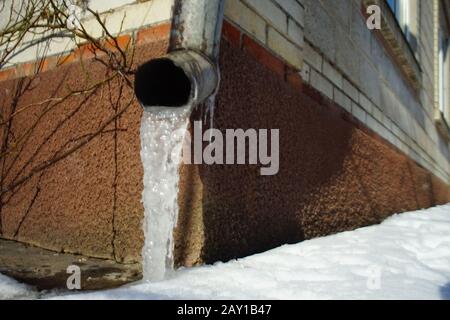 Drainpipe an der Hausecke mit Eis und Schnee. Stockfoto