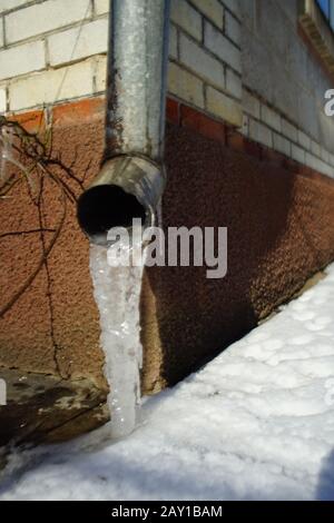 Drainpipe an der Hausecke mit Eis und Schnee auf dem Boden. Stockfoto