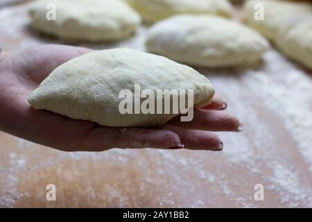 Auf der Handfläche einer Frau kochen gekochte Brötchen, die bereit zum Backen im Ofen sind. Tolles Dessert für Tee in der kalten Jahreszeit. Stockfoto