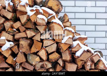 Gehacktes Brennholz, das unter einer Ziegelmauer gestapelt ist. Stockfoto