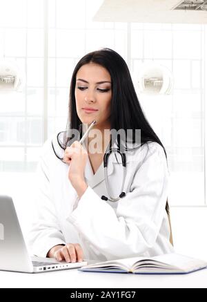 Junge Frau Doktor im weißen Mantel beim Computerdenken Stockfoto