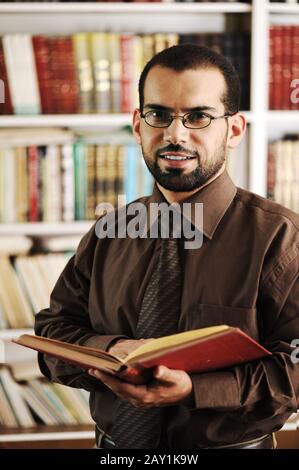 Junger glücklicher Mann, der in der Universitätsbibliothek liest und lächelt Stockfoto