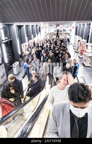 Menschenmassen auf einer internationalen Messe, die für Rolltreppen Schlange steht, von denen einige Masken tragen, um sich vor Coronavirus zu schützen Stockfoto