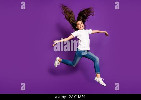 Ganzkörpergröße Blick auf sie schön fröhliche fröhliche, gewellte, gewellte Mädchen hüpft mit fließendem Wind, isoliert auf hellem, lebendigem Glanz Stockfoto