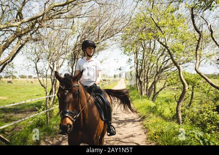 Kaukasische Frau, die ihr Pferd durch einen Weg reitet Stockfoto