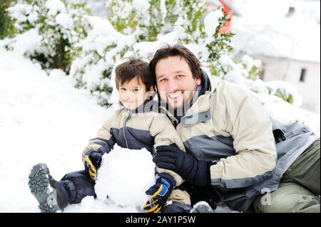 Vater und Sohn spielen glücklich im Schnee und machen Schneemann Stockfoto