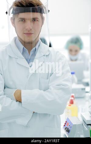 Selbstbewusster junger Arzt mit Maske und gefalteten Händen im Krankenhauslabor Stockfoto