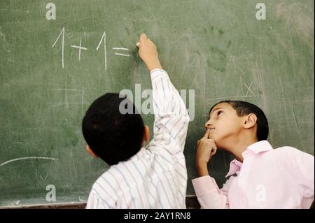 Zwei Jungen im Klassenzimmer denken, schreiben und an Bord zählen Stockfoto