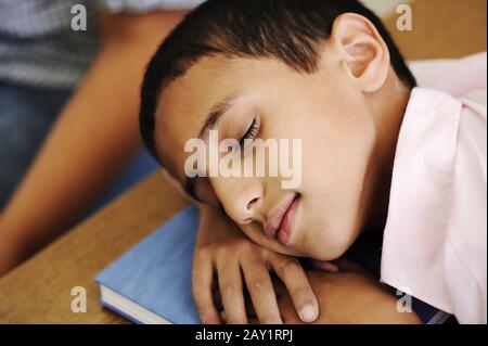 Kind im Klassenzimmer auf dem Schreibtisch, der auf seinem Notizbuch einschläft Stockfoto