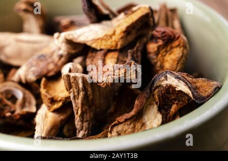 Nahaufnahme (Makro) von getrockneten Steinpilzen, die in einer grünen Keramikschale aufgehüpft sind. Stockfoto