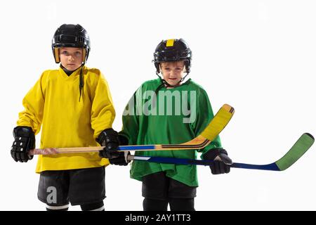 Kleine Eishockeyspieler mit den Stöcken auf dem Eisplatz und weißem Studiohintergrund. Sportsboys tragen Ausrüstung und Helmübung. Sportkonzept, gesunder Lebensstil, Bewegung, Bewegung, Action. Stockfoto