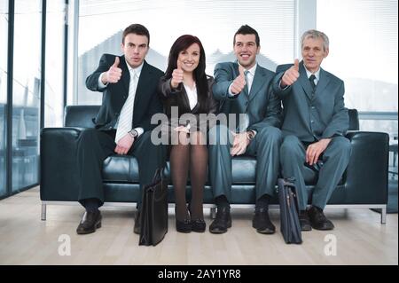Eine Gruppe von Geschäftsleuten, die mit Daumen nach oben auf dem Sofa sitzen Stockfoto