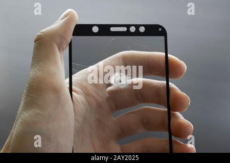 Zerbrochenes Schutzglas des Smartphones mit Rissen in der Hand auf schwarzem Hintergrund. Stockfoto