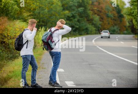 Wanderer auf der Straße. Reiseweg. Nur Freunde und weiter, spüren Sie die Freiheit. Reisen mit Freunden. Fahren Sie mit der Autostop. Hoffnungsloser Hexer. Männer versuchen, das Auto zu stoppen. Zwillinge gehen auf der Straße. Stockfoto