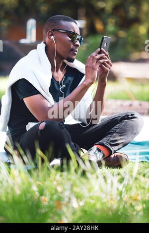 Kapstadt, Südafrika, 11. Mai - 2019: Mann sitzt im Park und schaut auf Telefon. Stockfoto