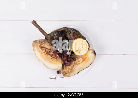 Melone, Weintrauben und Avocados auf einem weißen Teller mit Messer auf weißem Hintergrund, Konzept der Verschwendung von Lebensmitteln und Null Abfall Stockfoto