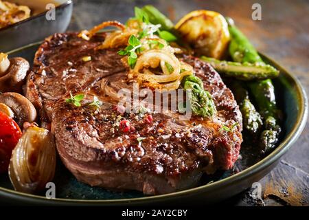 Saftiges gegrilltes Rindersteak, gewürzt mit Gewürzen und Kräutern, serviert mit frischen grünen Spargelspitzen, gerösteten Zwiebeln und Pilzen in Nahernte Stockfoto