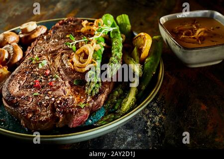 Frischer grüner Spargel serviert mit einem dicken saftigen gegrillten Rindersteak, gewürzt mit Gewürzen und Kräutern und Champignons auf der Seite in Nahaufnahme Stockfoto