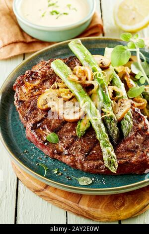 Gegrilltes Rumpsteak mit frischen grünen Spargelfrüchten und mit frischen Kräutern und Gewürzen garnierten Pilzen in Nahaufnahme Stockfoto