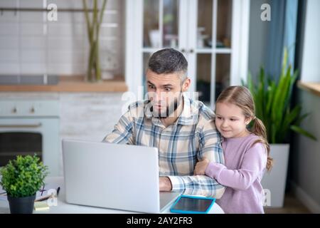 Junger dunkelhaariger Vater und Mädchen, die auf einen Laptop blicken. Stockfoto