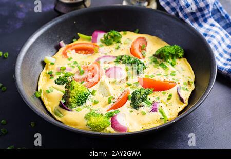 Omelette mit Brokkoli, Tomaten und roten Zwiebeln in Eisenkillet. Italienische Frittata mit Gemüse. Stockfoto