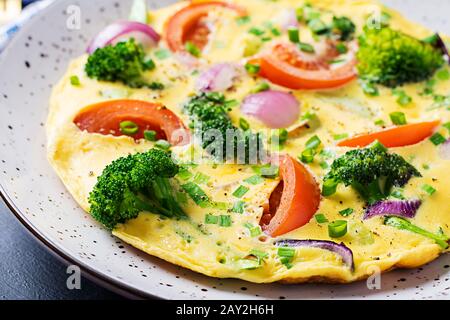 Omelette mit Brokkoli, Tomaten und roten Zwiebeln auf dunklem Tisch. Italienische Frittata mit Gemüse. Stockfoto