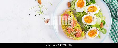 Frühstück. Gesundes, offenes Sandwich auf Toast mit Avocado und Lachs, gekochten Eiern, Kräutern, chia-Samen auf weißem Teller mit Kopierraum. Gesundes Protein fo Stockfoto