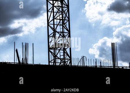 Dunkler bewölkter Himmel an der Baustelle Silhouettenkran. Investitionstätigkeit im sozialen Wohnungsbau oder Infrastruktur für Arbeitsarbeit. Stockfoto