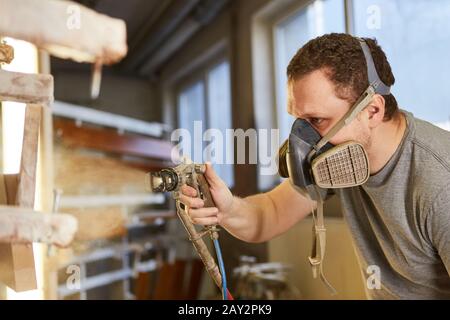 Varnisher lackiert Holz mit Gesichtsmaske und Brille im Zimmerei Stockfoto