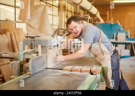 Tischlerlehrling arbeitet mit Holzbohlen an der Hobelmaschine in der Zimmerei Stockfoto