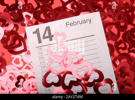 Kalenderseite geöffnet bis 14. Februar, Valentinstag umgeben von glänzenden Herzen auf rotem Hintergrund Stockfoto