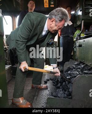 Alan Titchmarsh schaufelt Kohle in den Kessel auf der Fußplatte des Flying Scotsman, nachdem es am Bahnhof Alton in Hampshire angekommen war, um die Watercress Line der Mid Hants Railway nach Abschluss der Arbeiten an Der Butts Bridge offiziell wieder zu eröffnen. Stockfoto