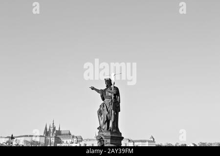 Isolierte religiöse Statue mit Kruzifix in der Karlsbrücke mit dem Schloss im Hintergrund (Prag, Tschechien, Europa) Stockfoto