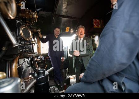 Alan Titchmarsh chattet mit Mitgliedern der Besatzung auf der Fußplatte des Flying Scotsman, nachdem es am Bahnhof Alton in Hampshire angekommen war, um die Watercress Line der Mid Hants Railway nach Abschluss der Arbeiten an Butts Bridge offiziell wieder zu eröffnen. Stockfoto