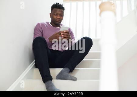Teenager-Junge, Der Durch Sms Auf Einer Treppe Zu Hause Sitzt, Schikaniert Wird Stockfoto